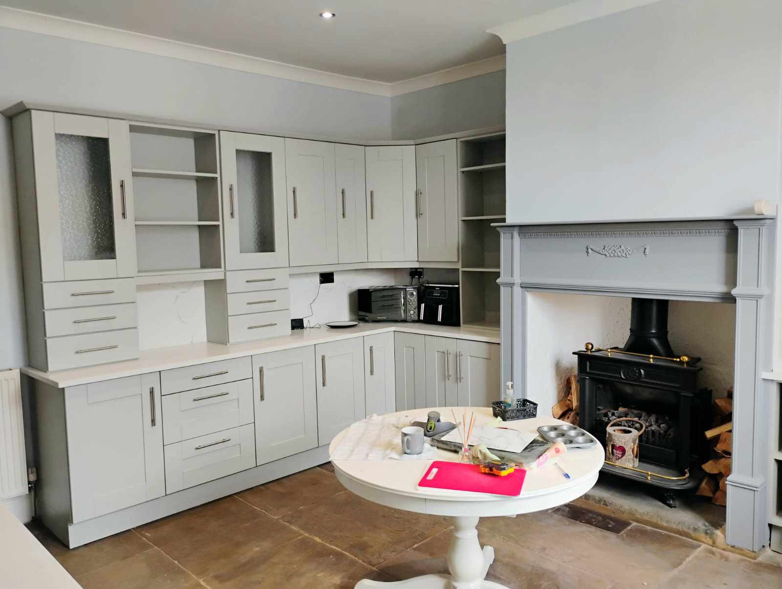 Light grey shaker-style kitchen units after spray painting, beside a painted fire surround